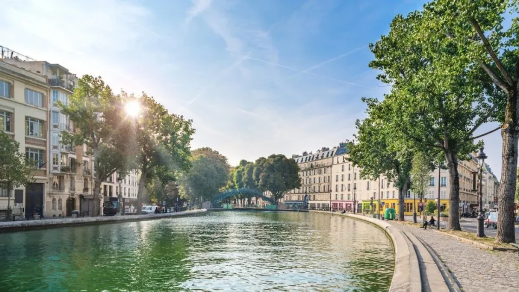 A charming view of Canal Saint-Martin in Paris, France, featuring tree-lined waterways, quaint bridges, and historic buildings. The scene captures the picturesque and serene atmosphere of this popular Parisian neighborhood.