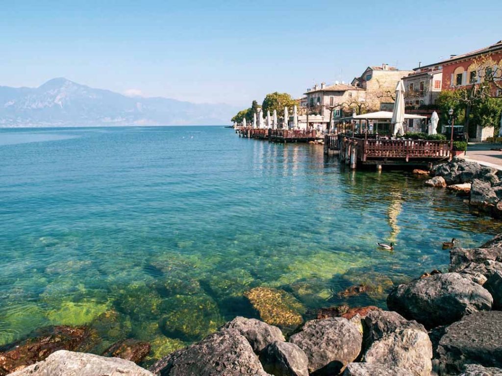 A stunning view of Lake Garda in Italy, featuring crystal-clear waters surrounded by picturesque hills and charming lakeside towns. The image highlights the natural beauty and tranquil ambiance of this popular Italian destination.