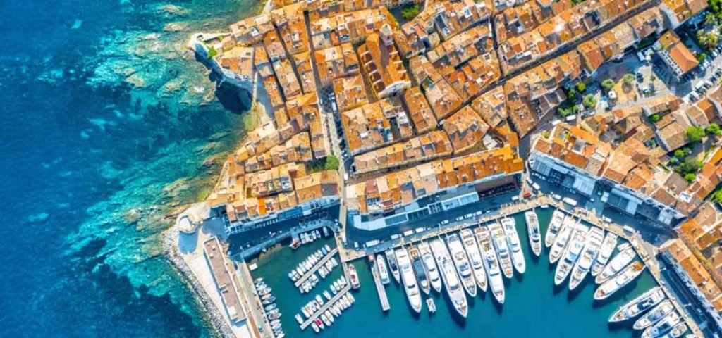 A picturesque view of St. Tropez, France, showcasing its charming harbor filled with luxury yachts, colorful buildings, and clear blue skies. The image captures the elegant and vibrant atmosphere of this renowned French Riviera destination.