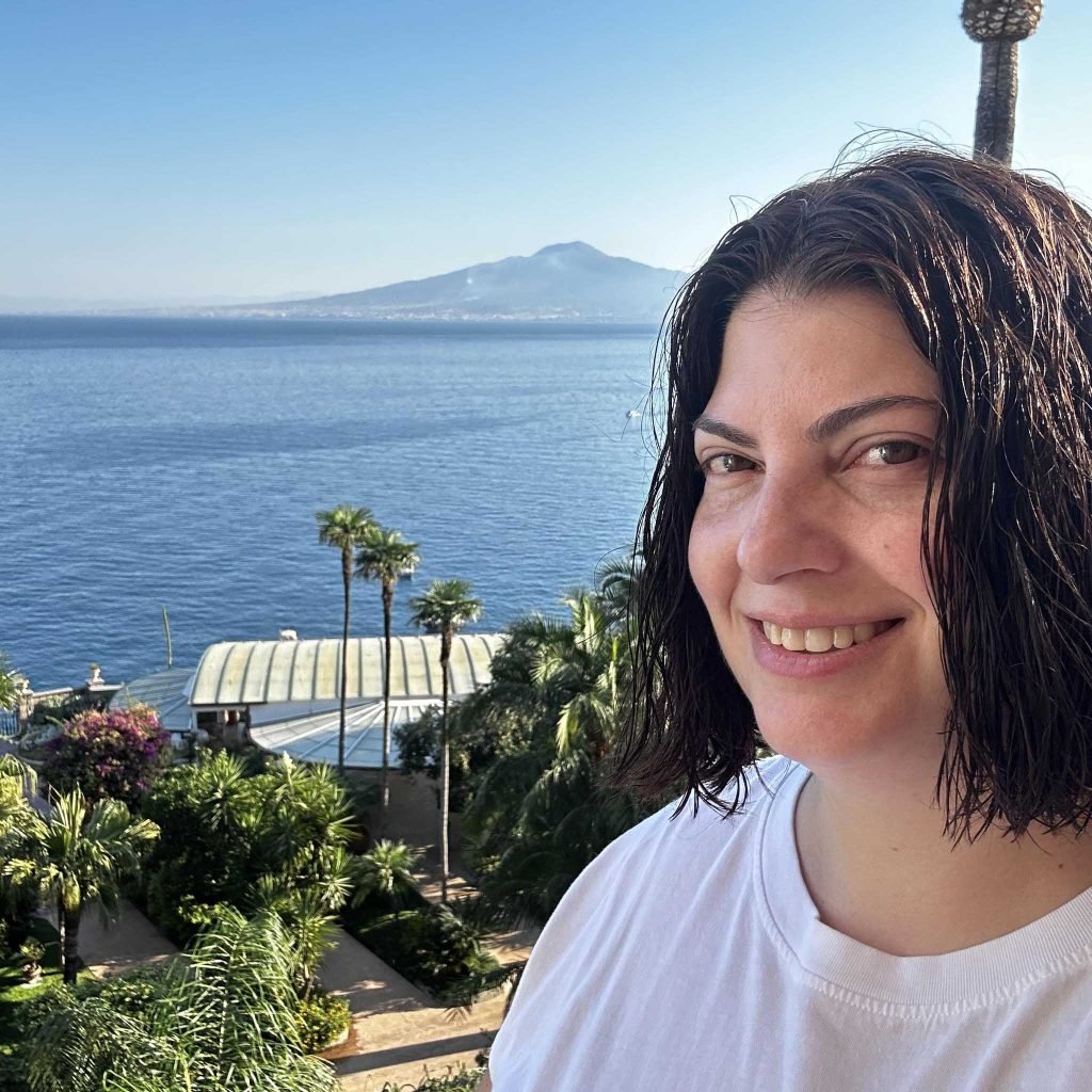 A professional portrait of Tamara, a Fora Travel Advisor from New Jersey, with a backdrop showcasing a world map or travel-themed decor. The image conveys expertise and a personalized approach to travel planning.